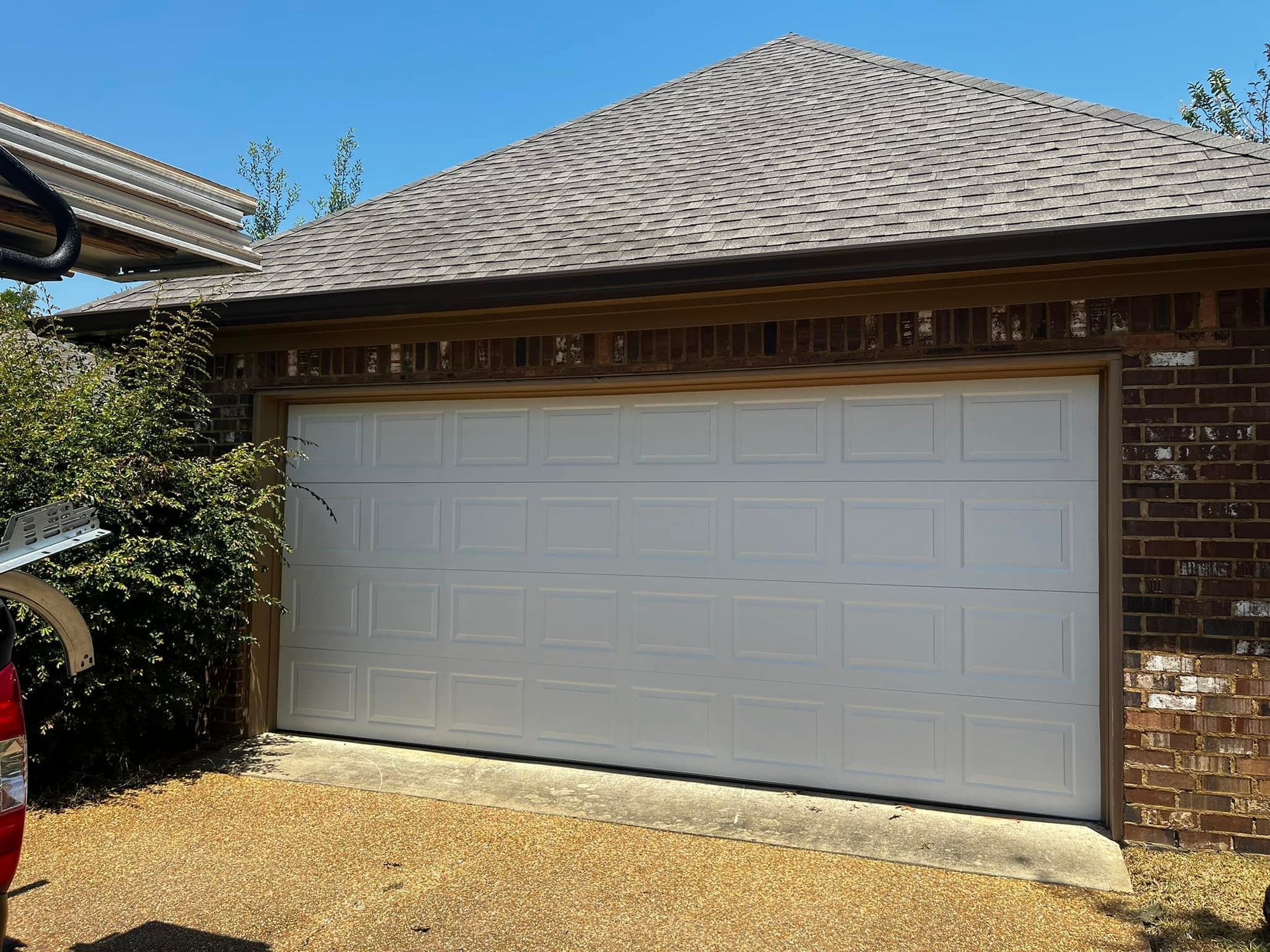 A white garage door is sitting in front of a brick house.