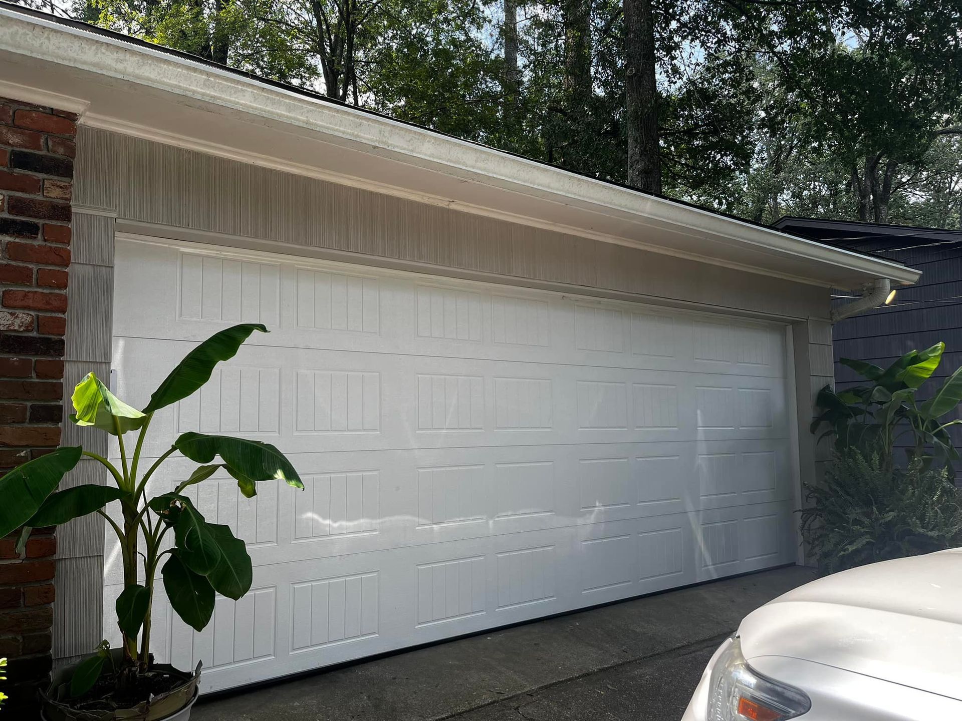 A white car is parked in front of a white garage door.