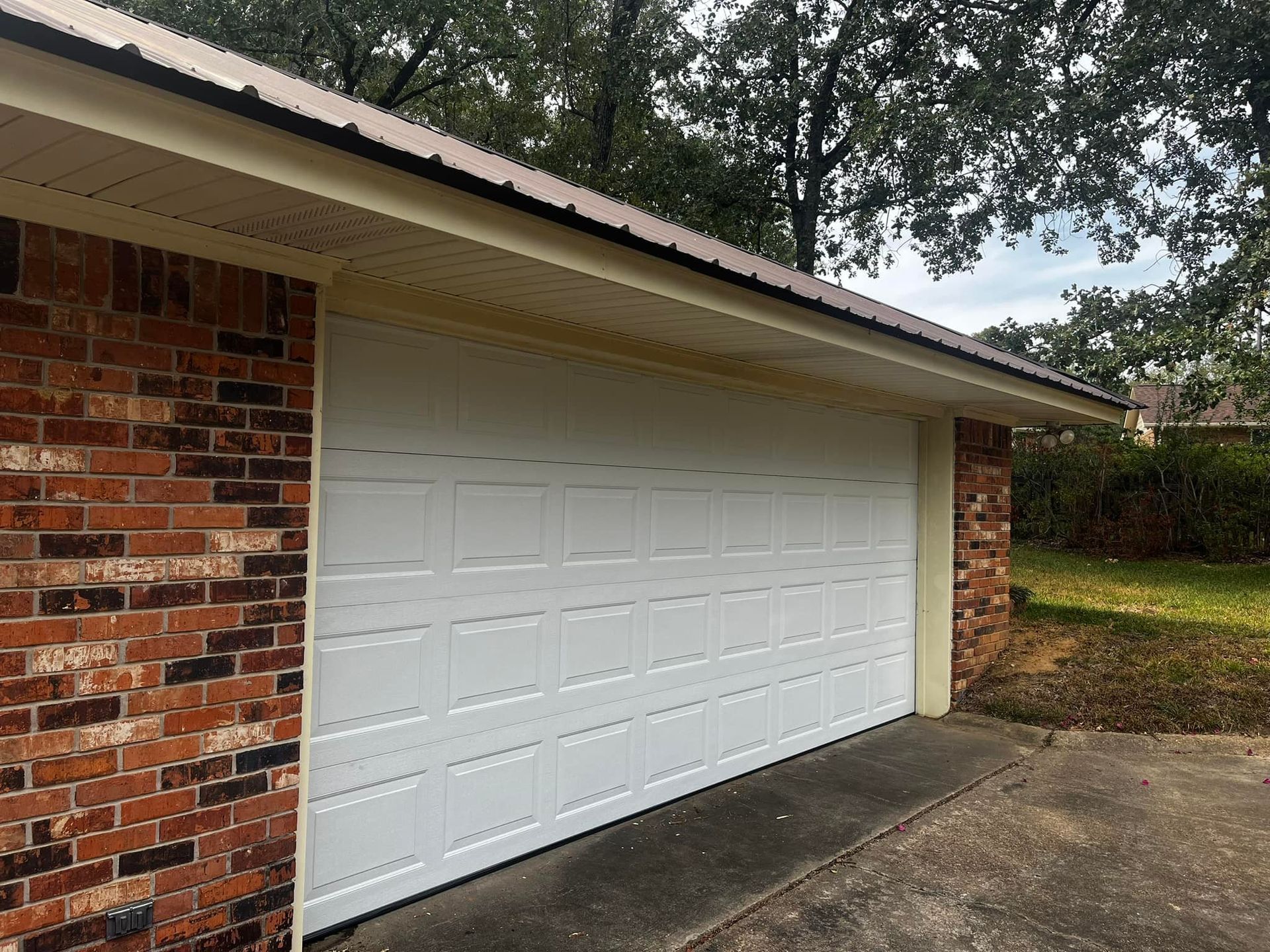 A white garage door is sitting in front of a brick building.