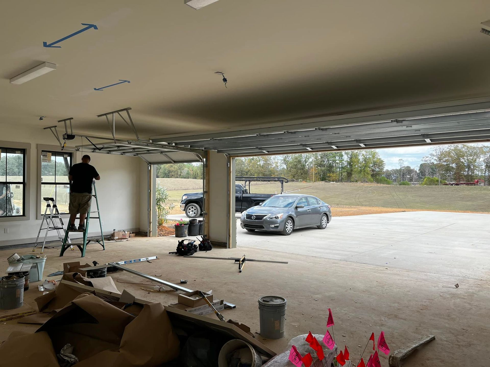 A man is standing on a ladder in a garage with a car parked in the background.