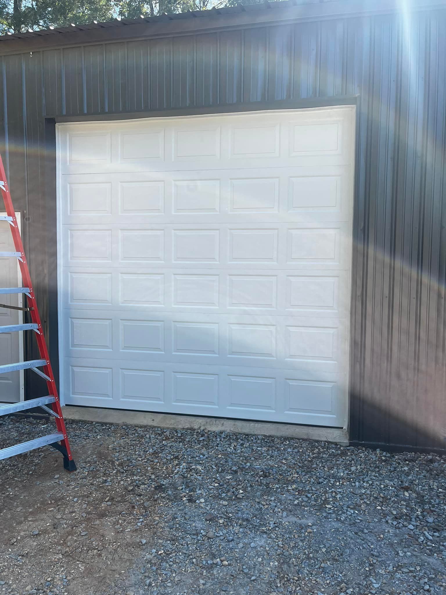 A white garage door is sitting on top of a gravel driveway next to a ladder.
