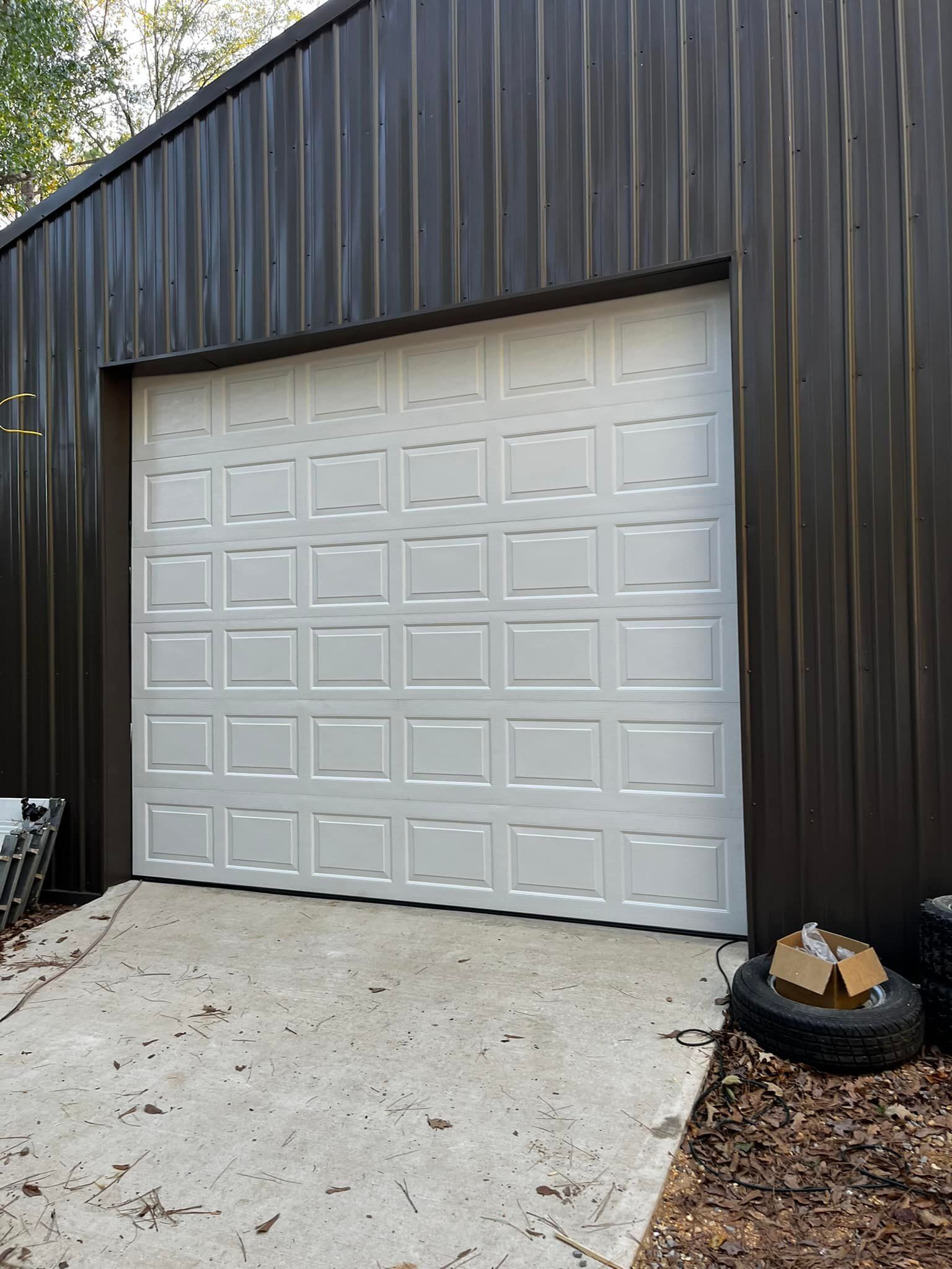 A white garage door is sitting in front of a black building.