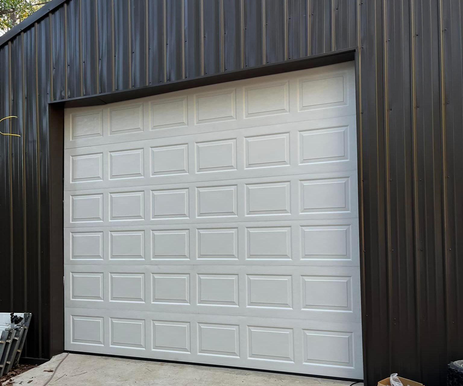 A white garage door is sitting in front of a black building.
