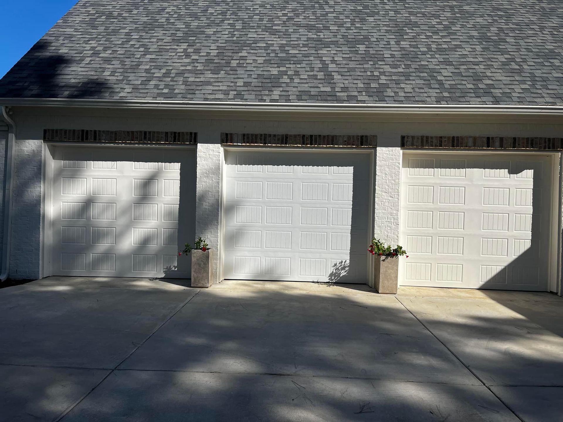 A garage with three white garage doors and a gray roof.