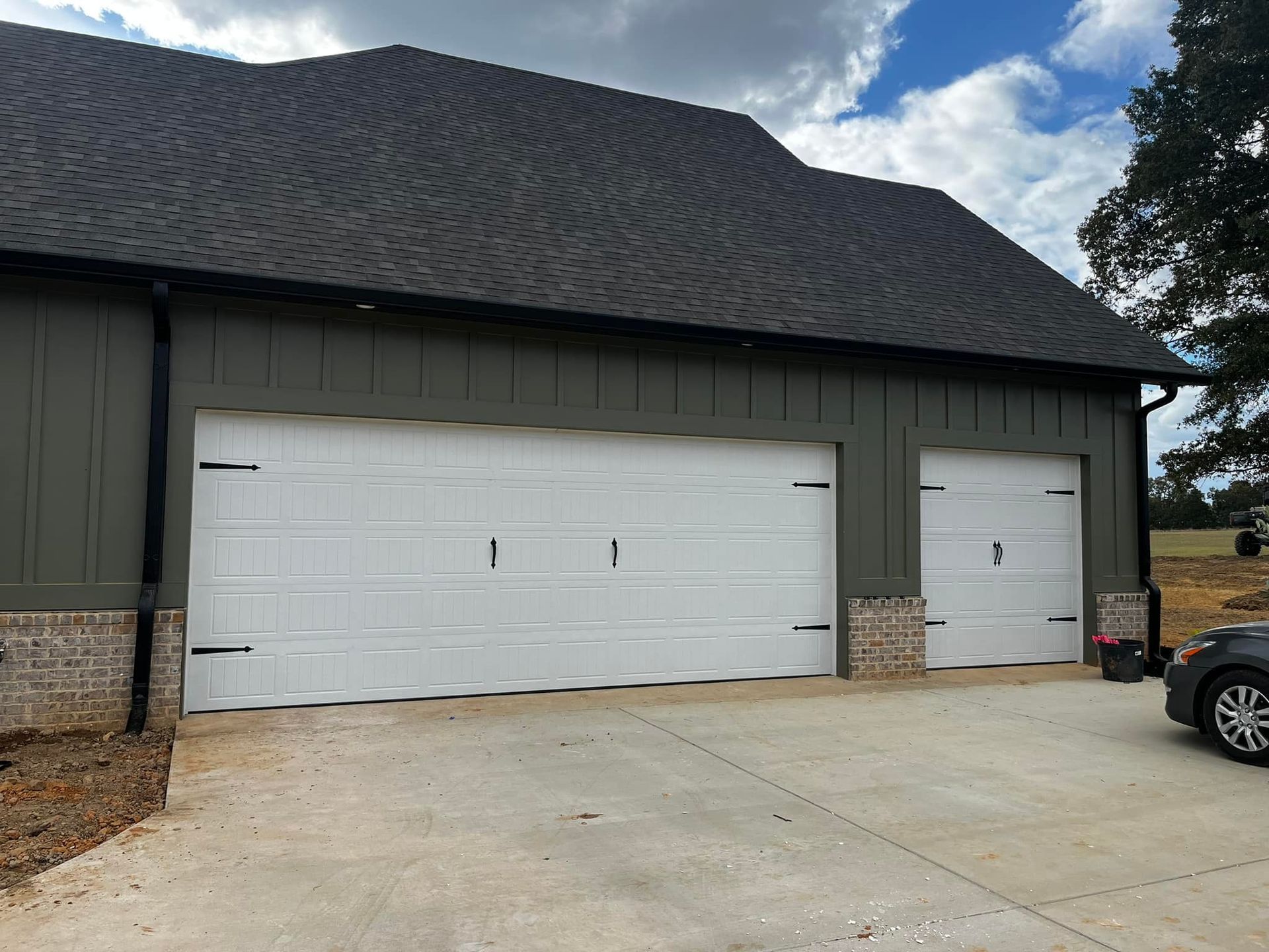 A car is parked in front of a garage with three white garage doors.
