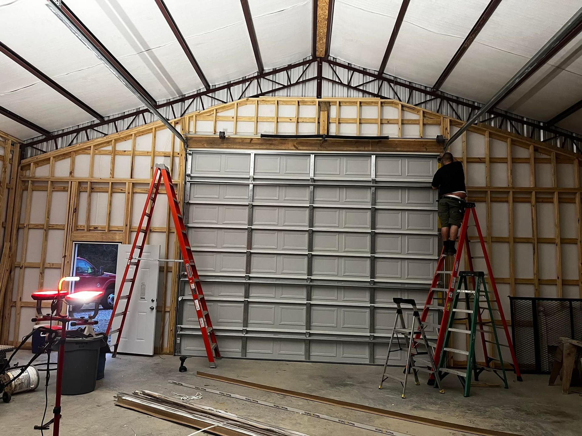 A man is standing on a ladder in a garage working on a garage door.