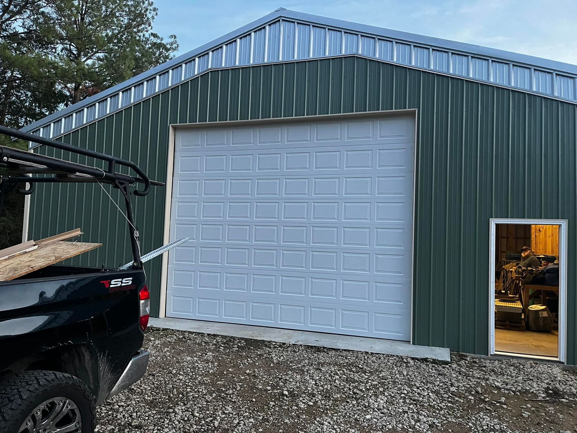 A truck is parked in front of a green garage with a white garage door.