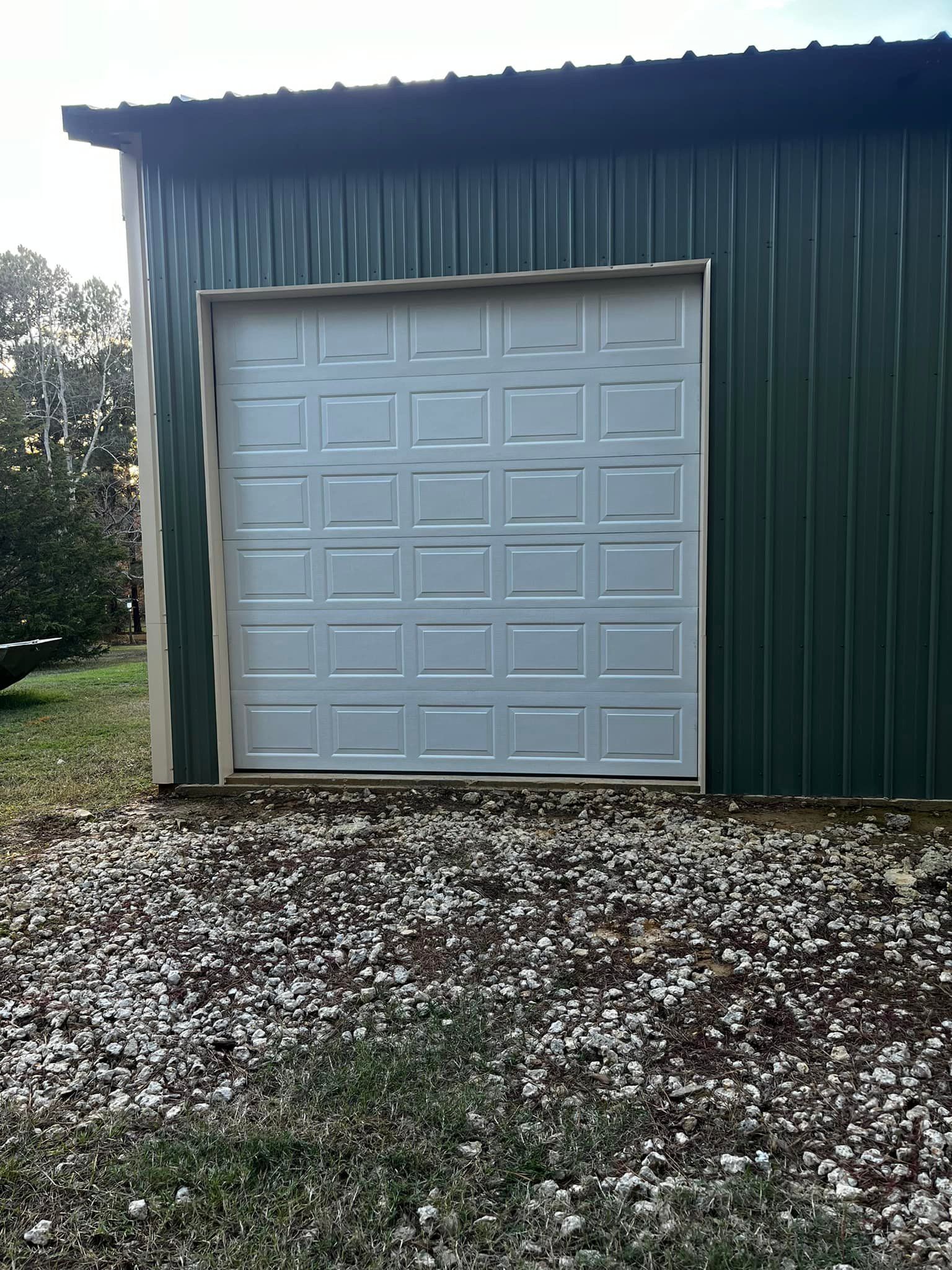 A white garage door is sitting on the side of a green building.