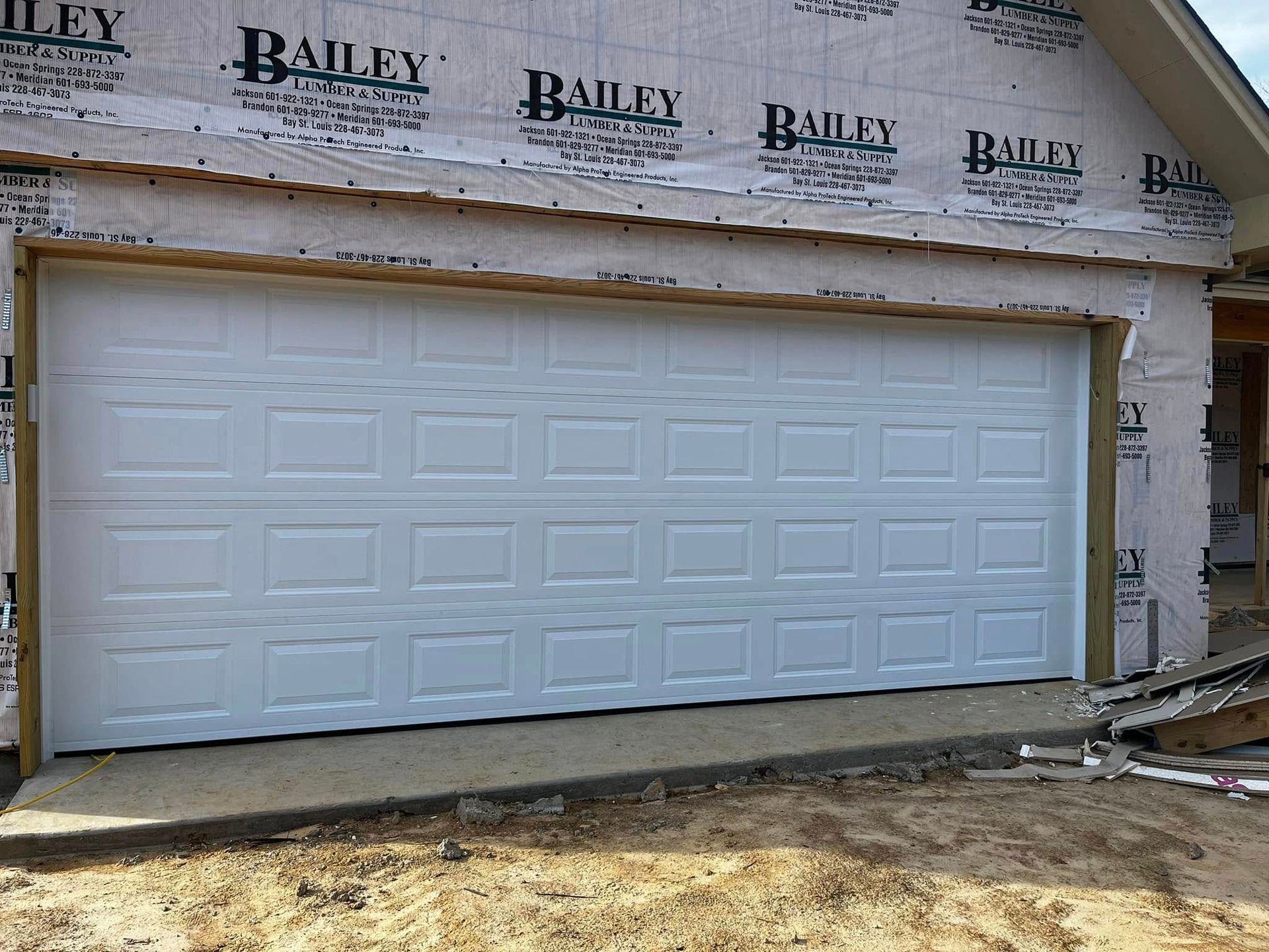 A white garage door is sitting in front of a house under construction.
