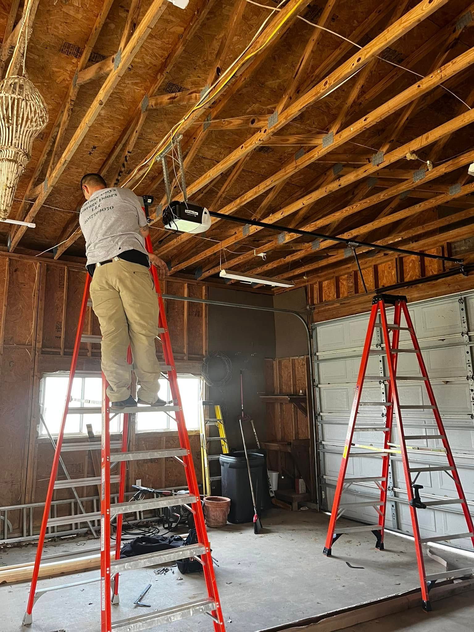 A man is standing on a ladder in a garage working on a garage door opener.