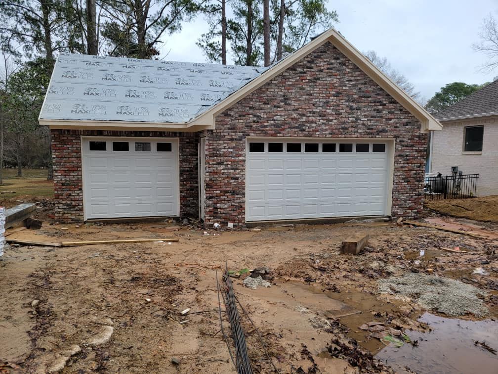 A brick garage with two white garage doors is being built.