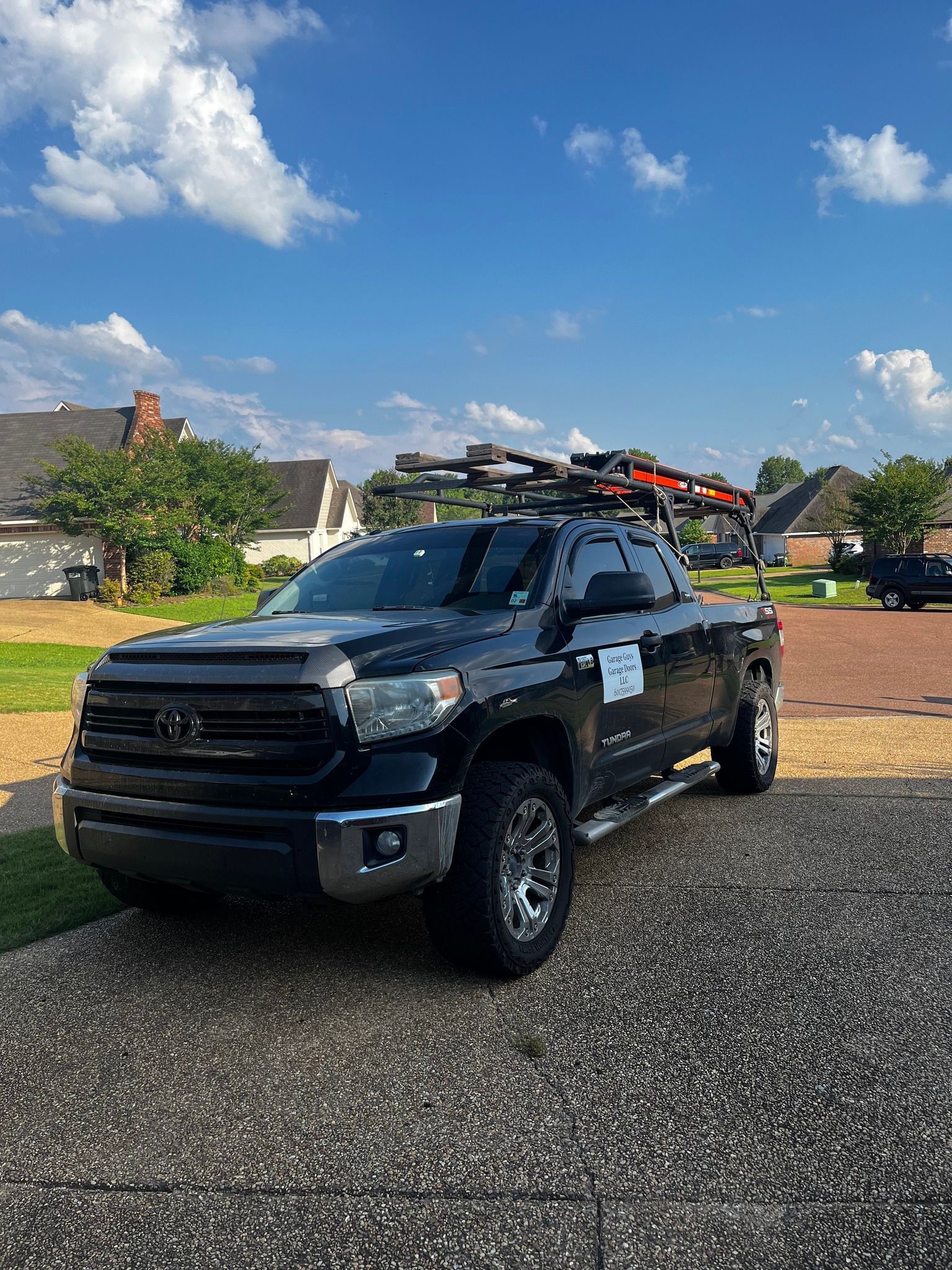 A black truck with skis on the roof is parked in a driveway.