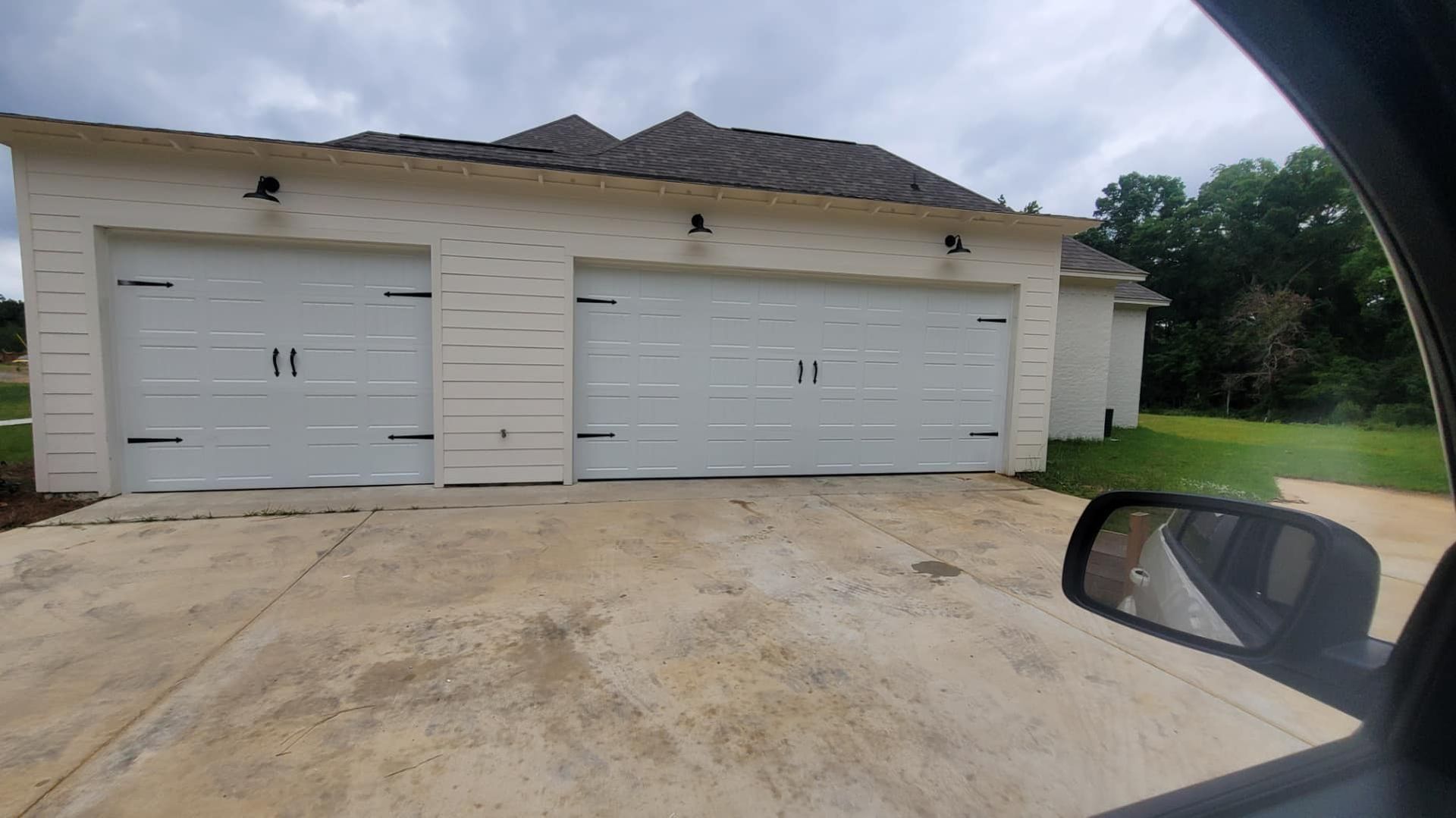 A car is parked in front of a garage with three garage doors.