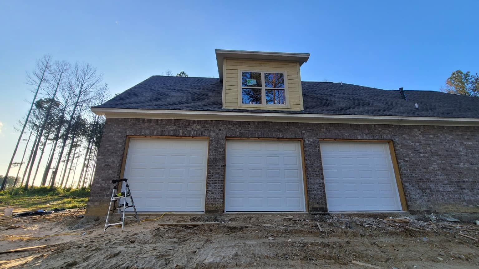A house with three garage doors and a ladder in front of it.