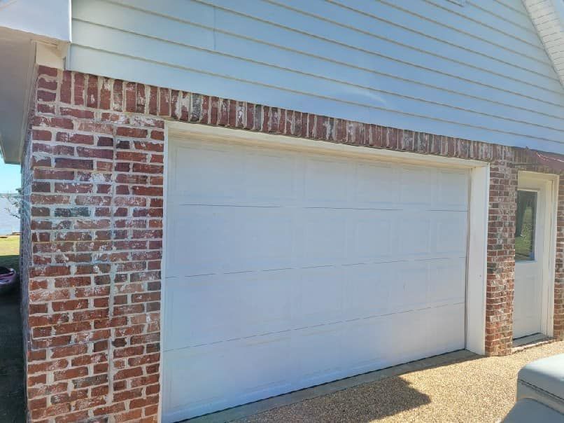 A white garage door is next to a red brick wall.
