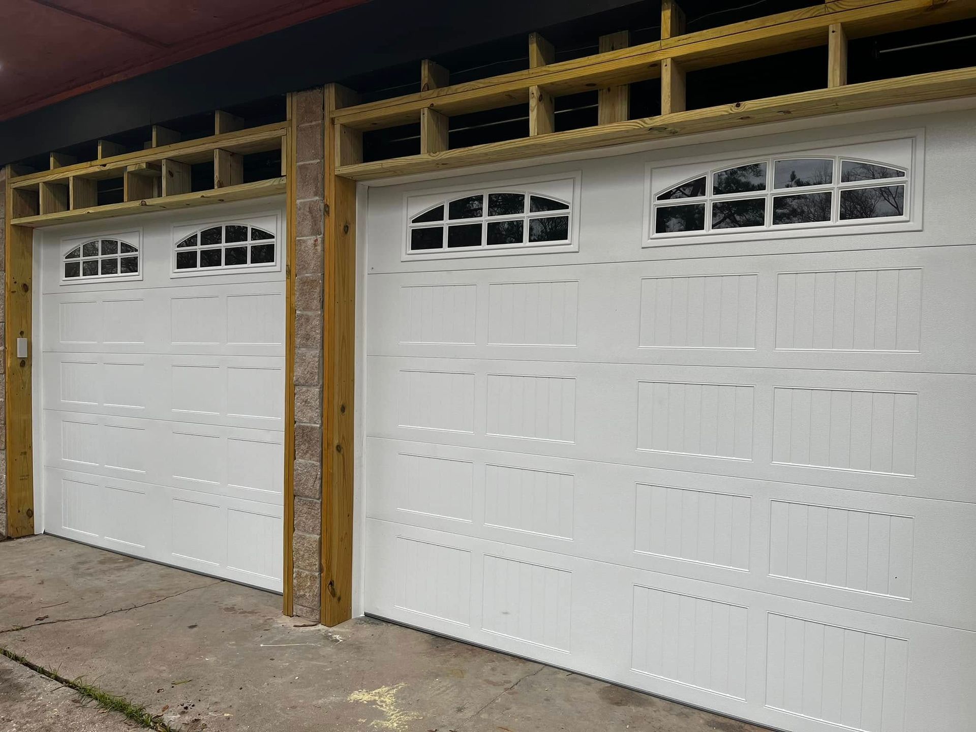 A pair of white garage doors with windows under construction.