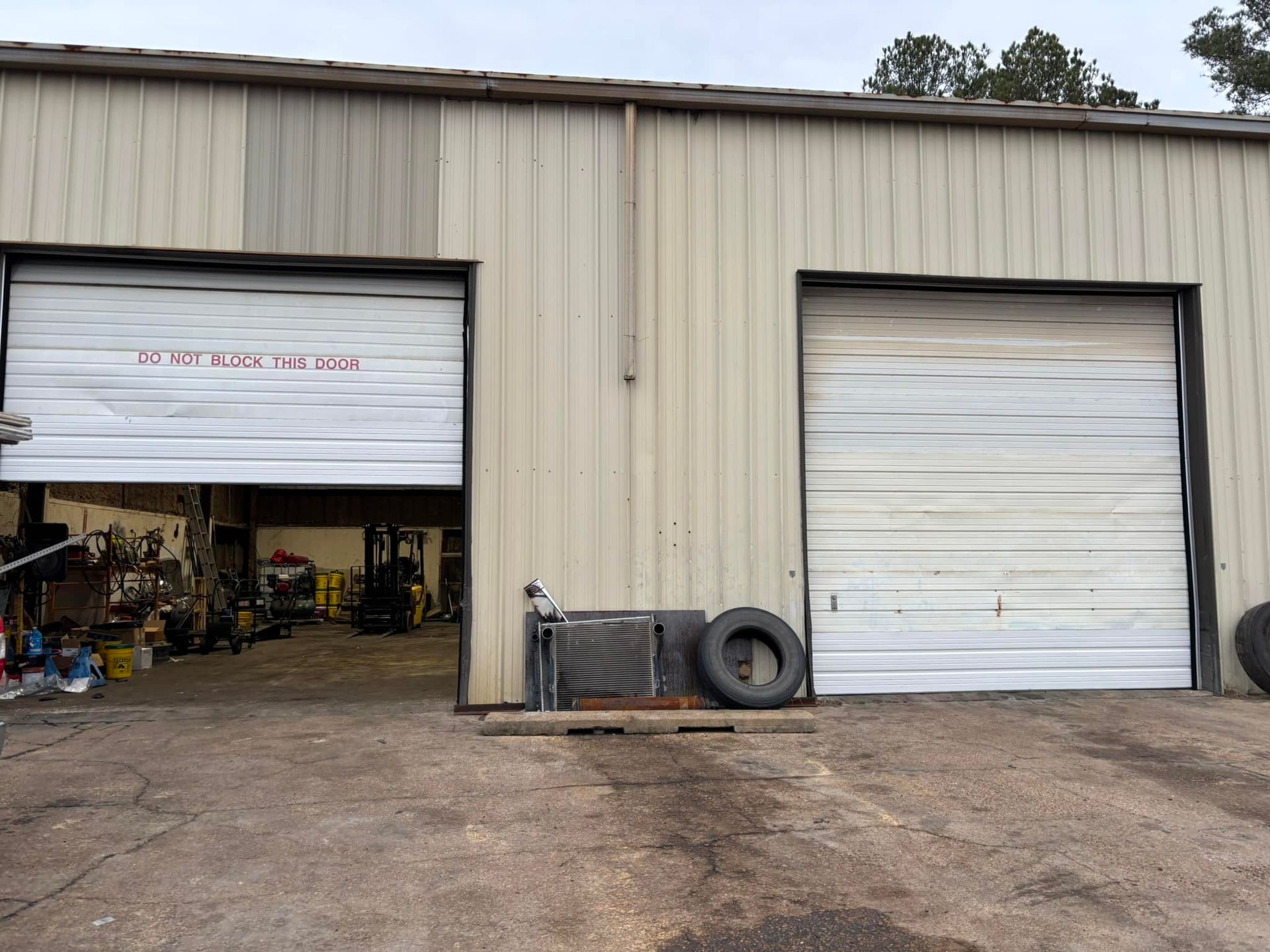 A garage with two garage doors open and a tire in front of it.