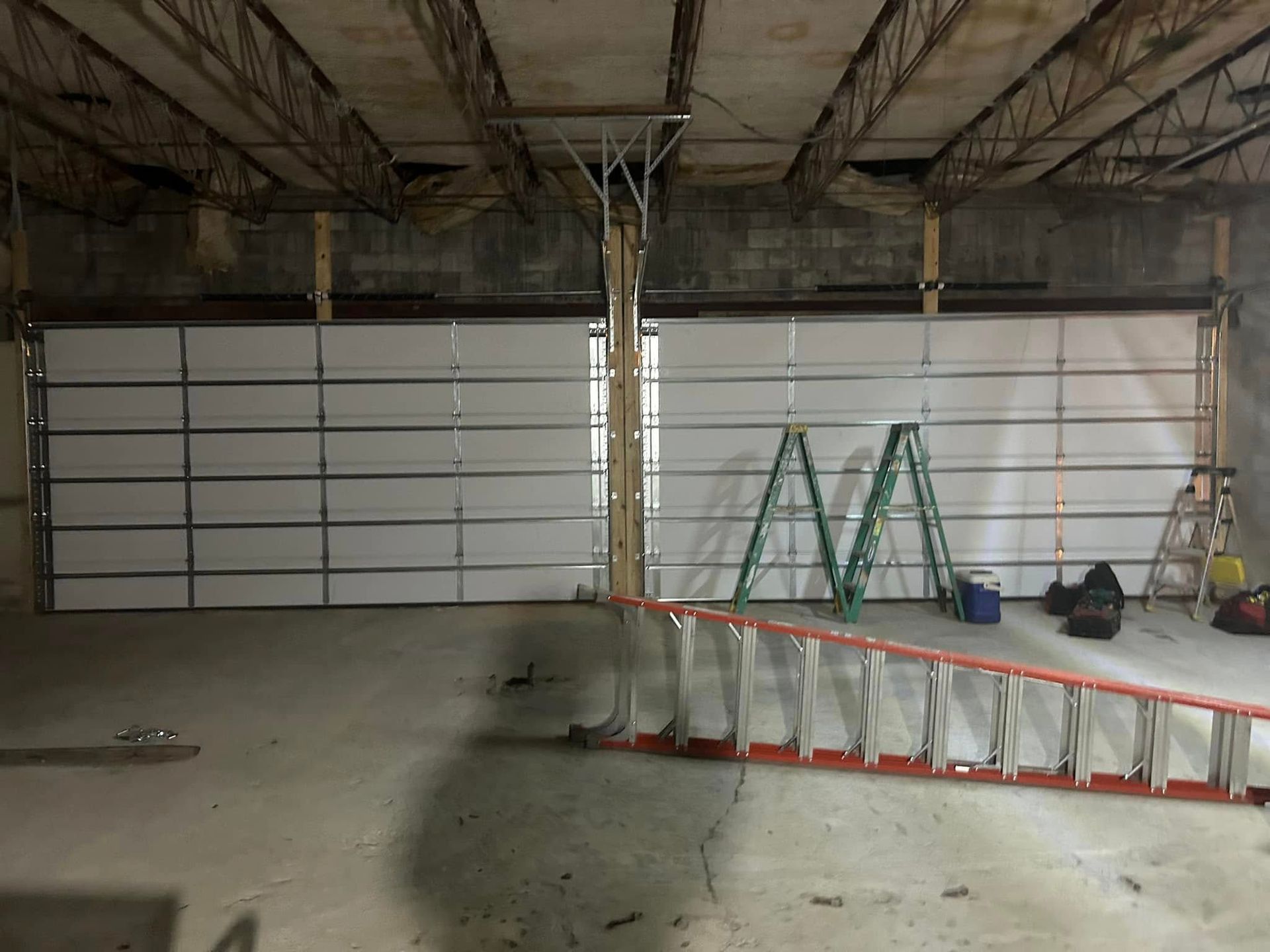 A garage door is being installed in a building with a ladder.