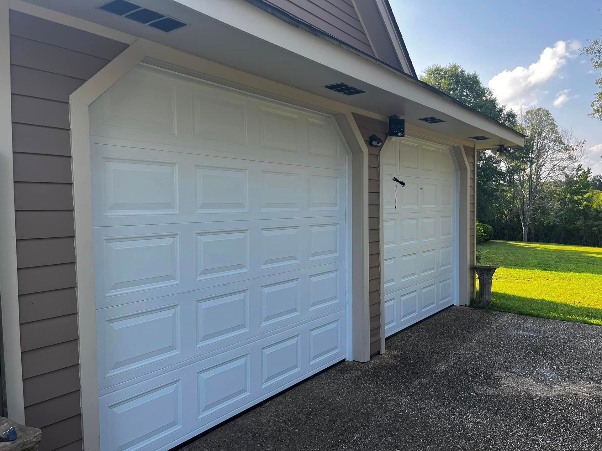 Two white garage doors are sitting next to each other on the side of a house.