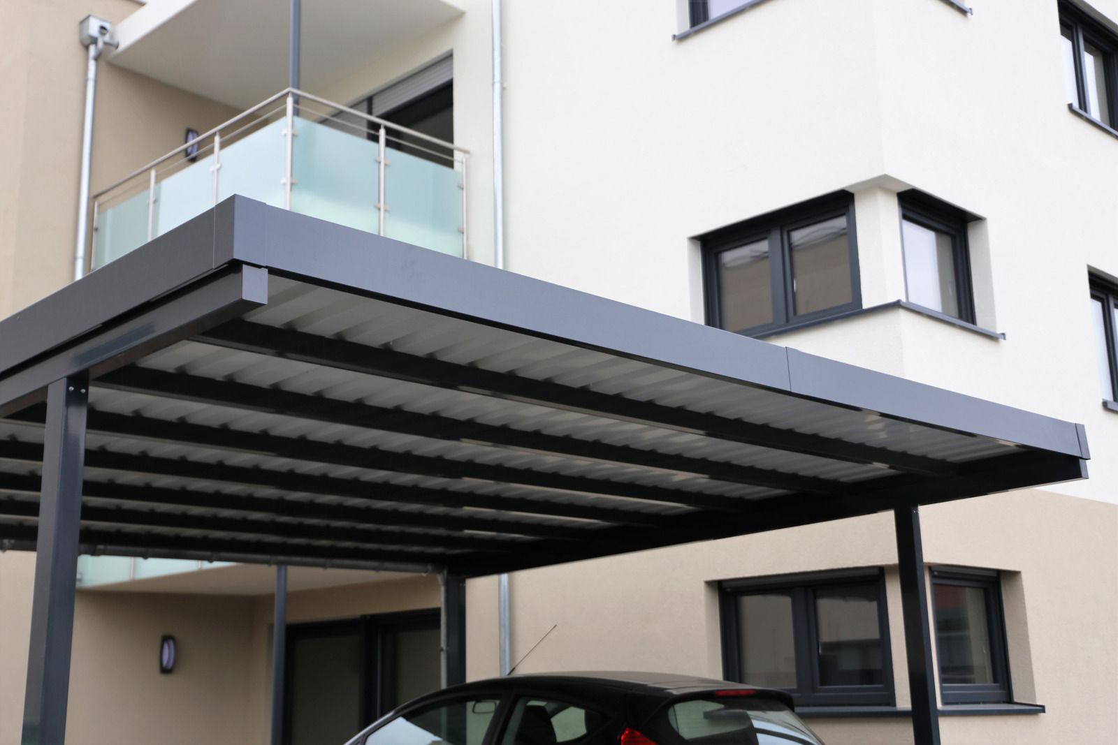 A car is parked under a carport in front of a building.