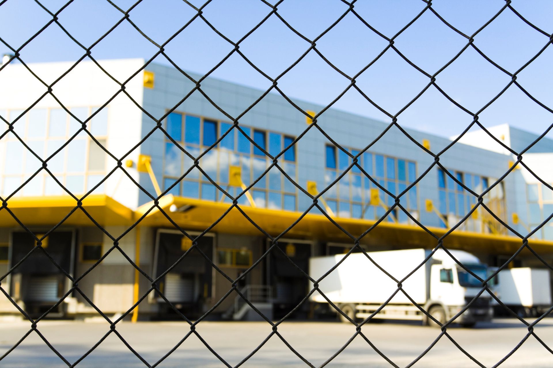 Commercial fence securing loading dock area with trucks at modern industrial warehouse facility.