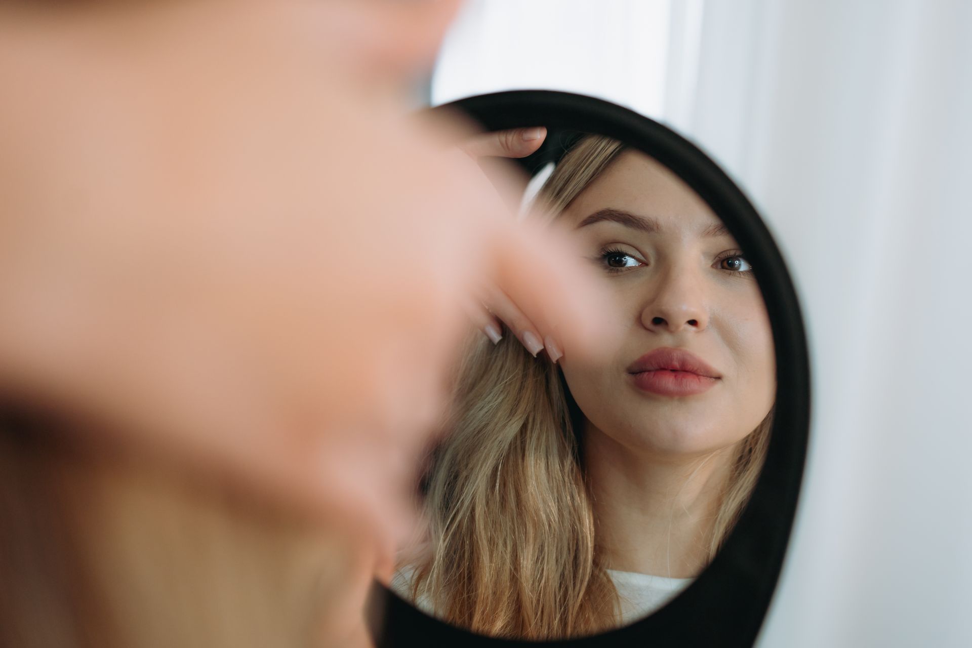 young woman looking in a mirror after facial rejuvenation procedure.