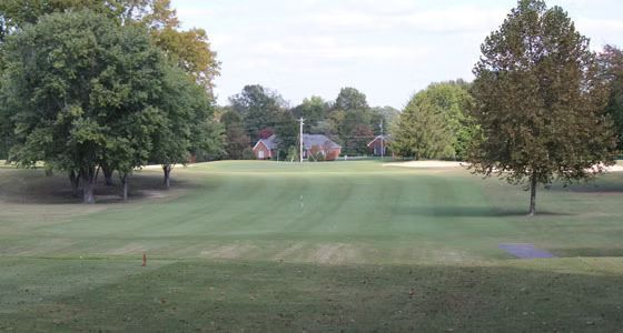 A golf course with trees and a house in the background