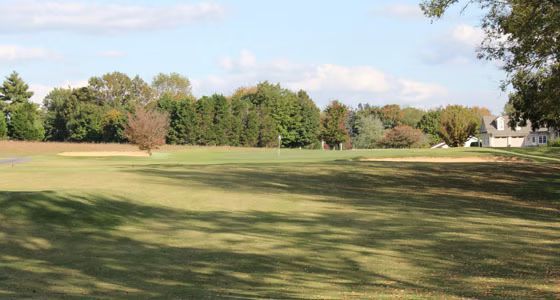 A large grassy field with trees in the background and a house in the distance.