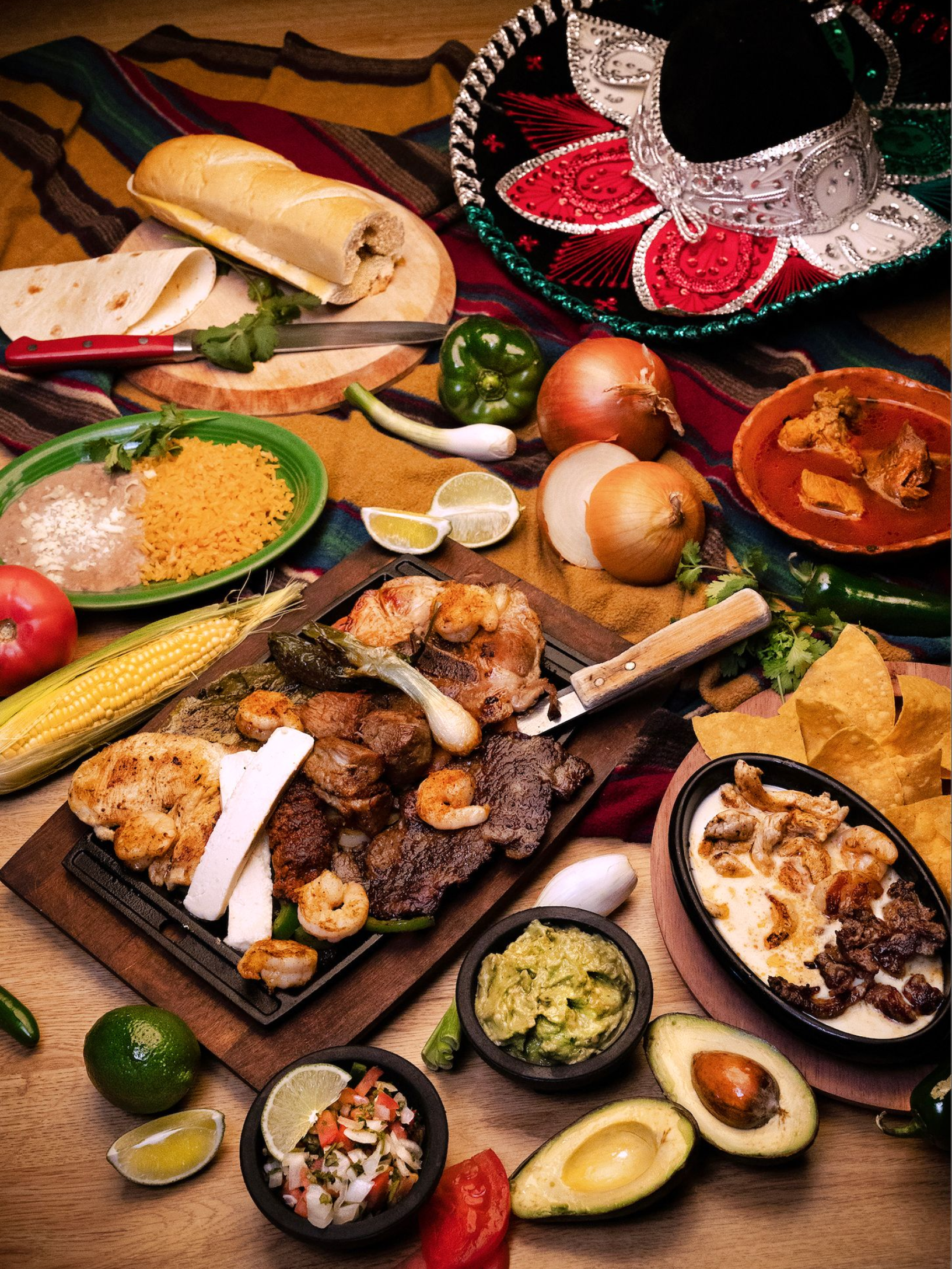 Mexican food spread: fajitas, tortillas, beans, rice, chips, guacamole, salsa, sombrero.