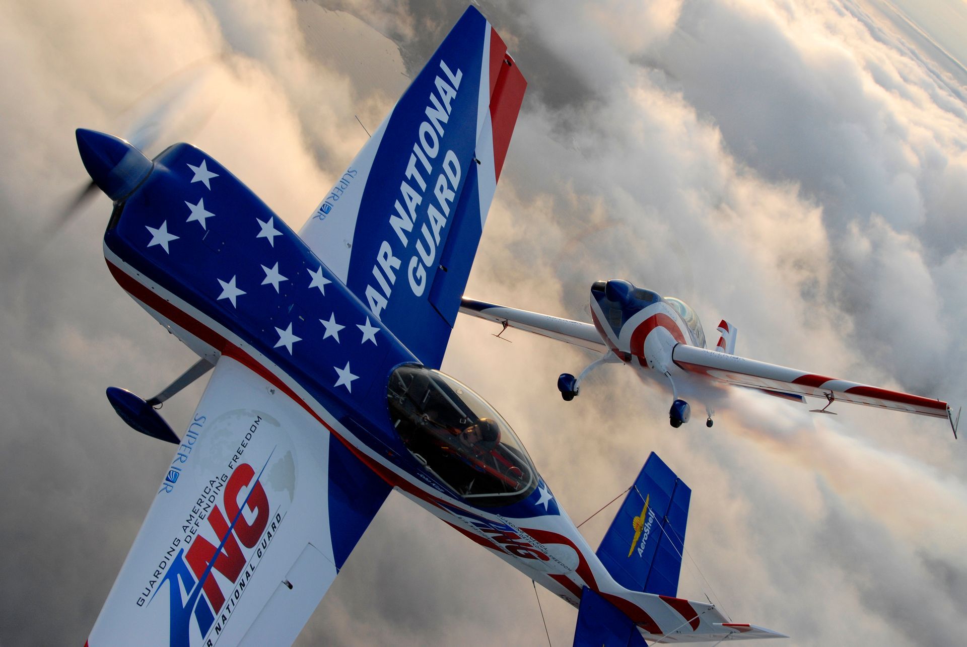 Two Air National Guard aerobatic planes fly close together against a cloudy sky; one is inverted.