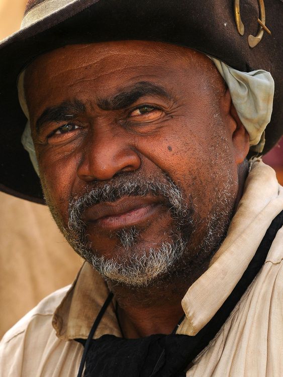 Man wearing a hat and light-colored shirt, looking directly at the camera with a slight smile.