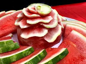 Watermelon slices and carved watermelon flower arrangement on a plate. Red, green, and white colors.