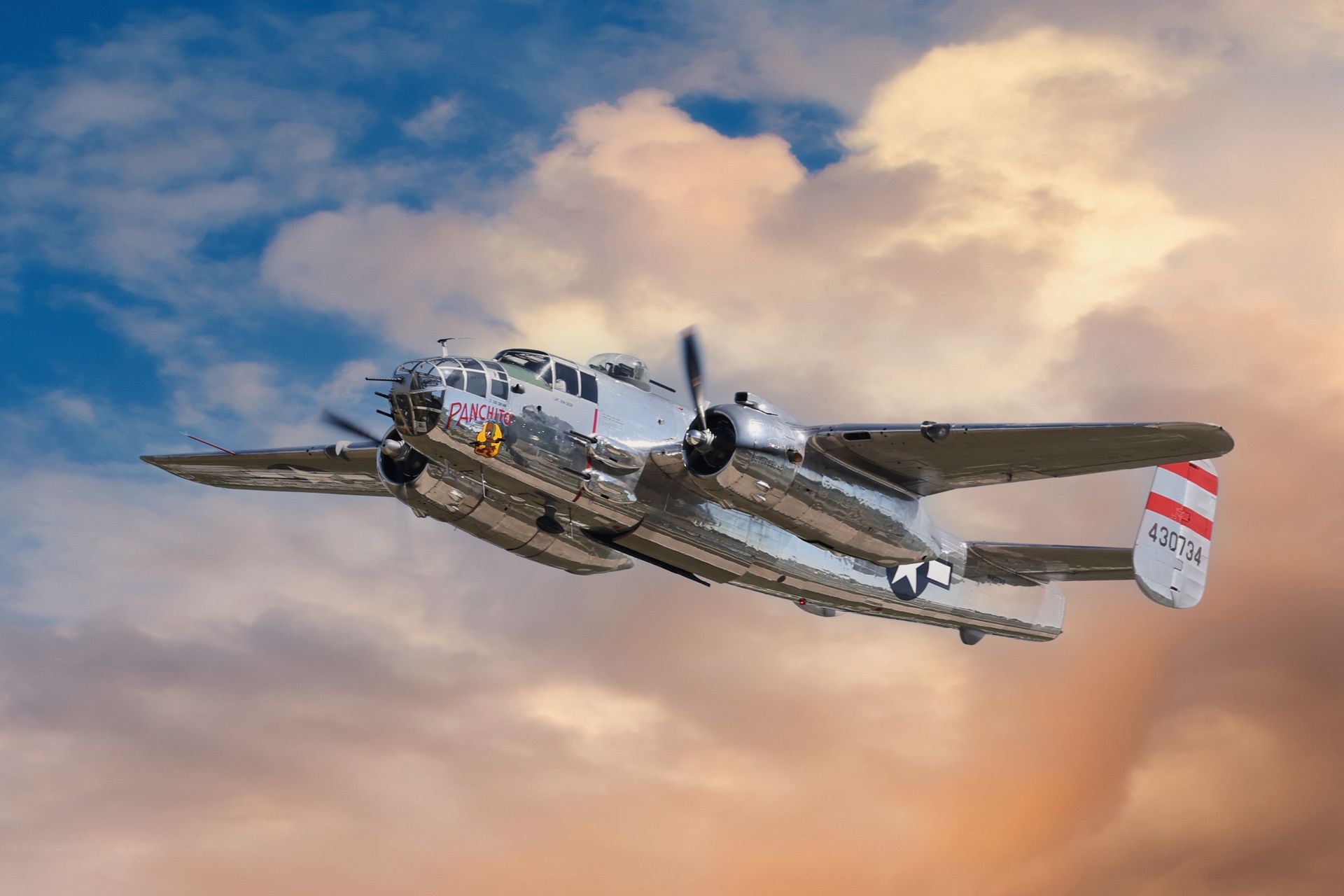 Silver B-25 Mitchell bomber aircraft in flight against a cloudy sky, red and white tail fin.