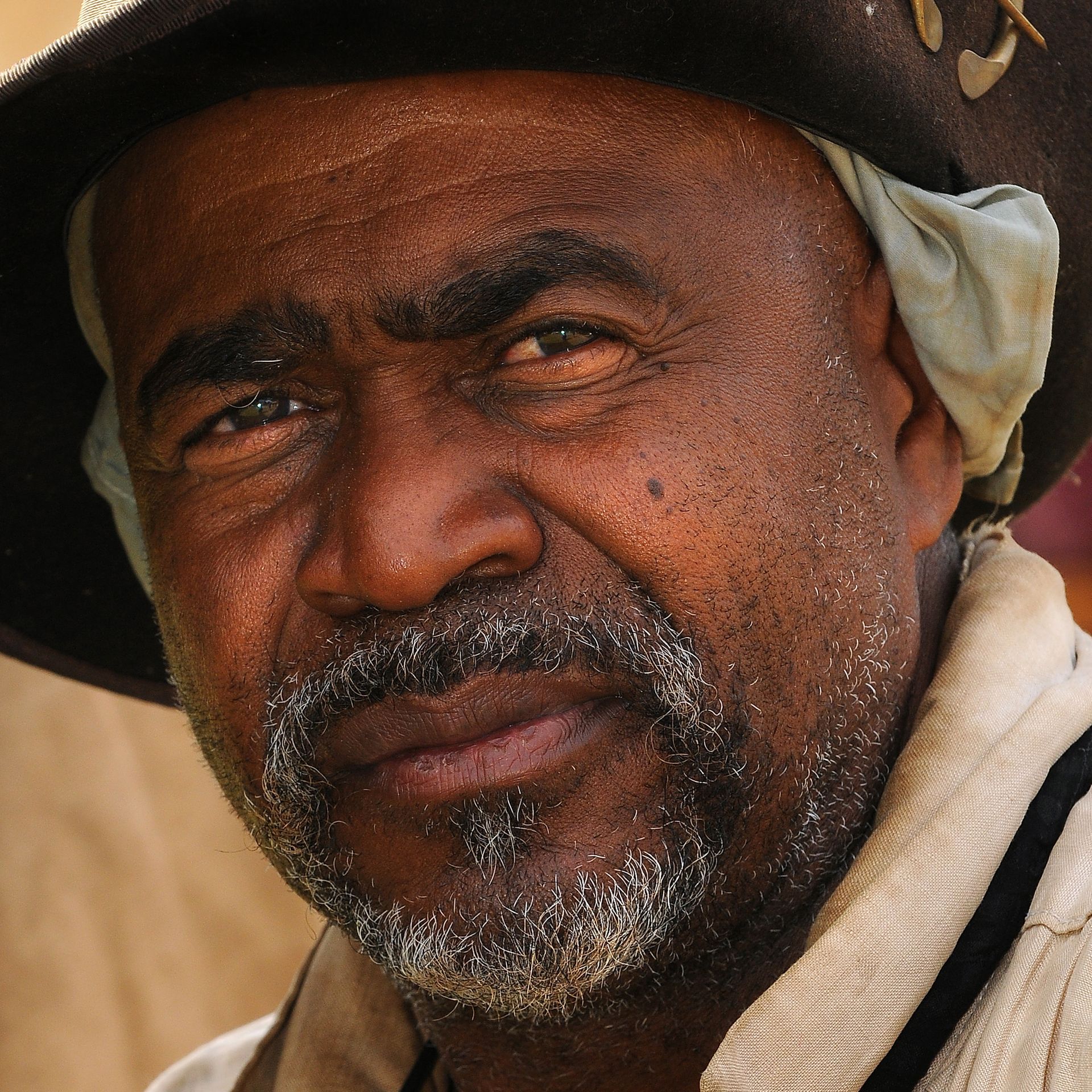 Man with dark skin, wearing hat, looking at the camera. He has a graying beard and a slight smile.