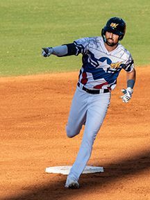 Baseball player running towards base; wearing a star-patterned jersey, helmet, and light gray pants.