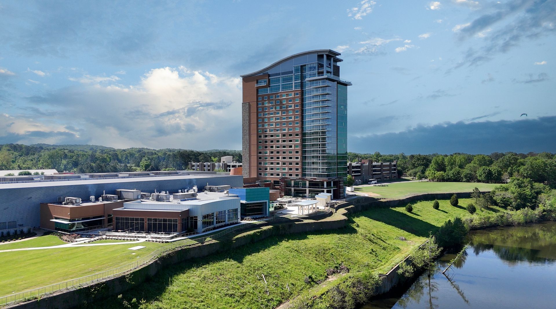 Modern hotel building with a glass facade, next to a grassy lawn and lake.