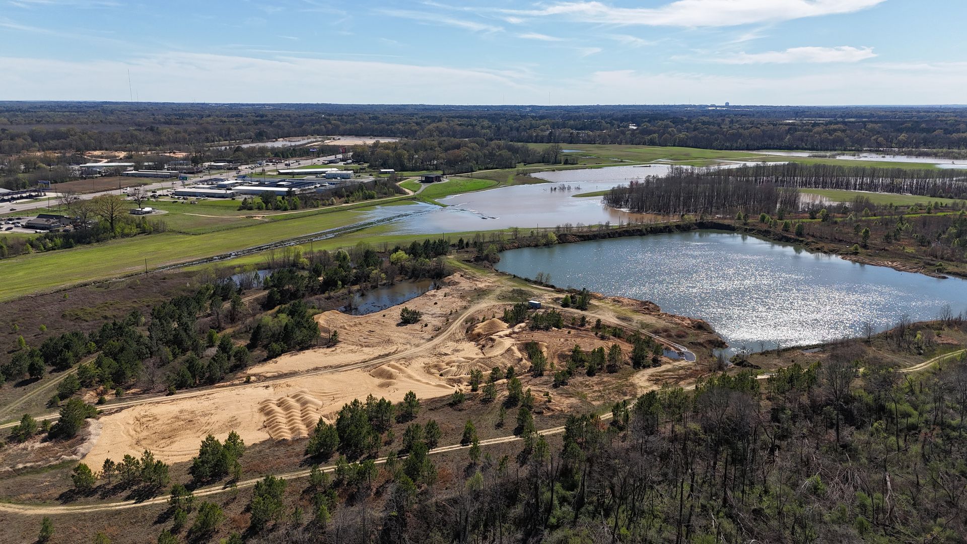 Aerial view of a landscape with lakes, green fields, and patches of trees under a blue sky.