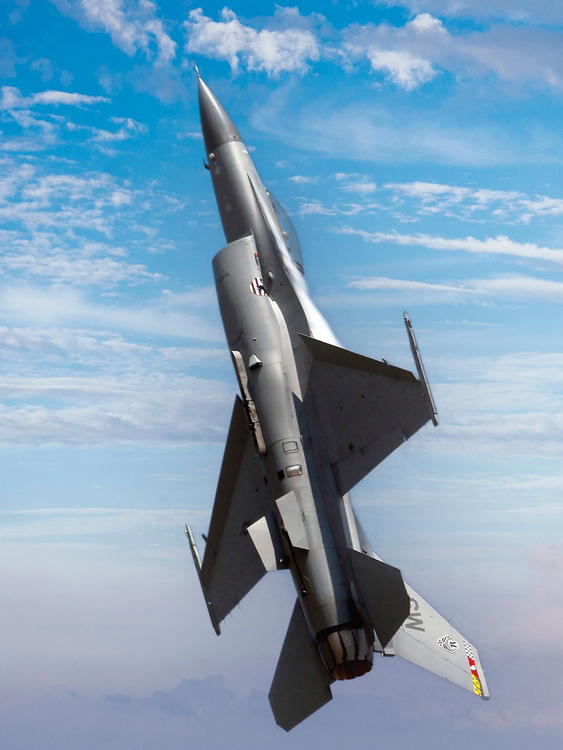 Gray fighter jet angled upward against a partly cloudy sky.