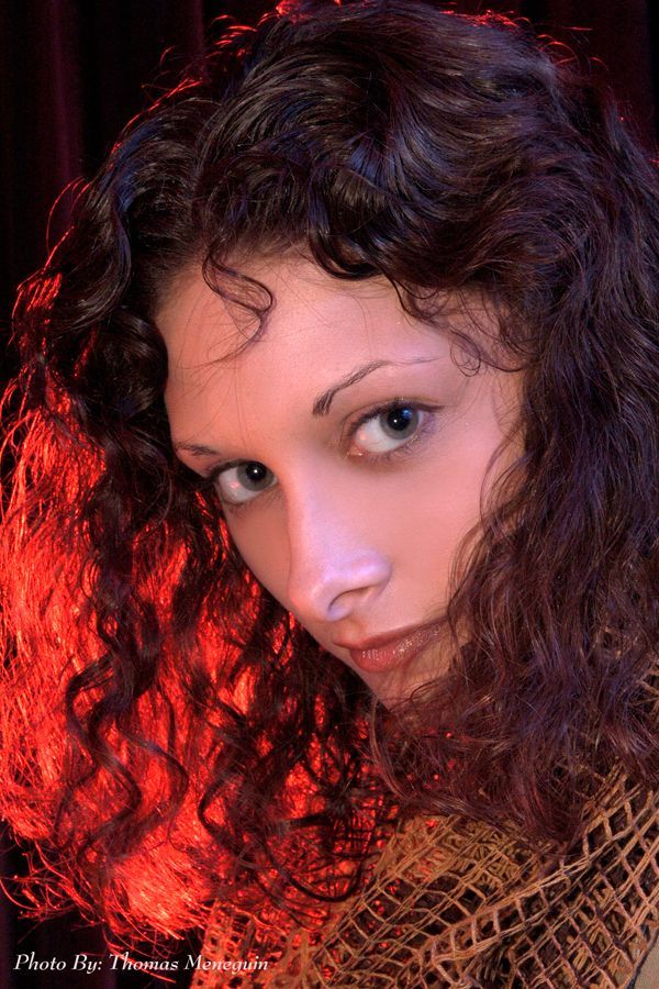 Woman with blonde hair, gray eyes, and red lipstick smiling, wearing a hoop earring. Blue background.