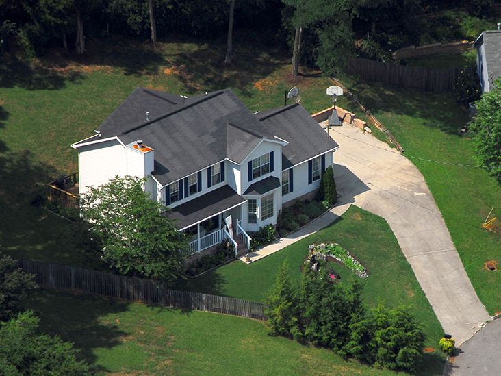 House with white siding and dark roof, set on a grassy hill with a long driveway.