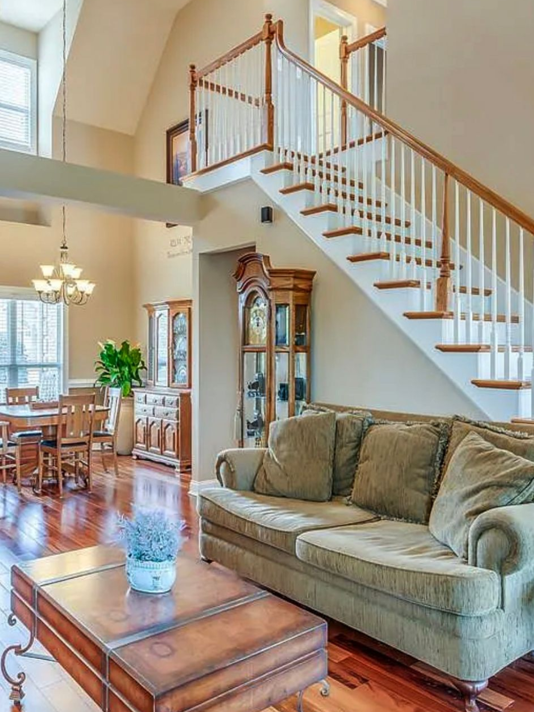 Living room with a sofa, staircase, and a dining area, hardwood floors, light walls.