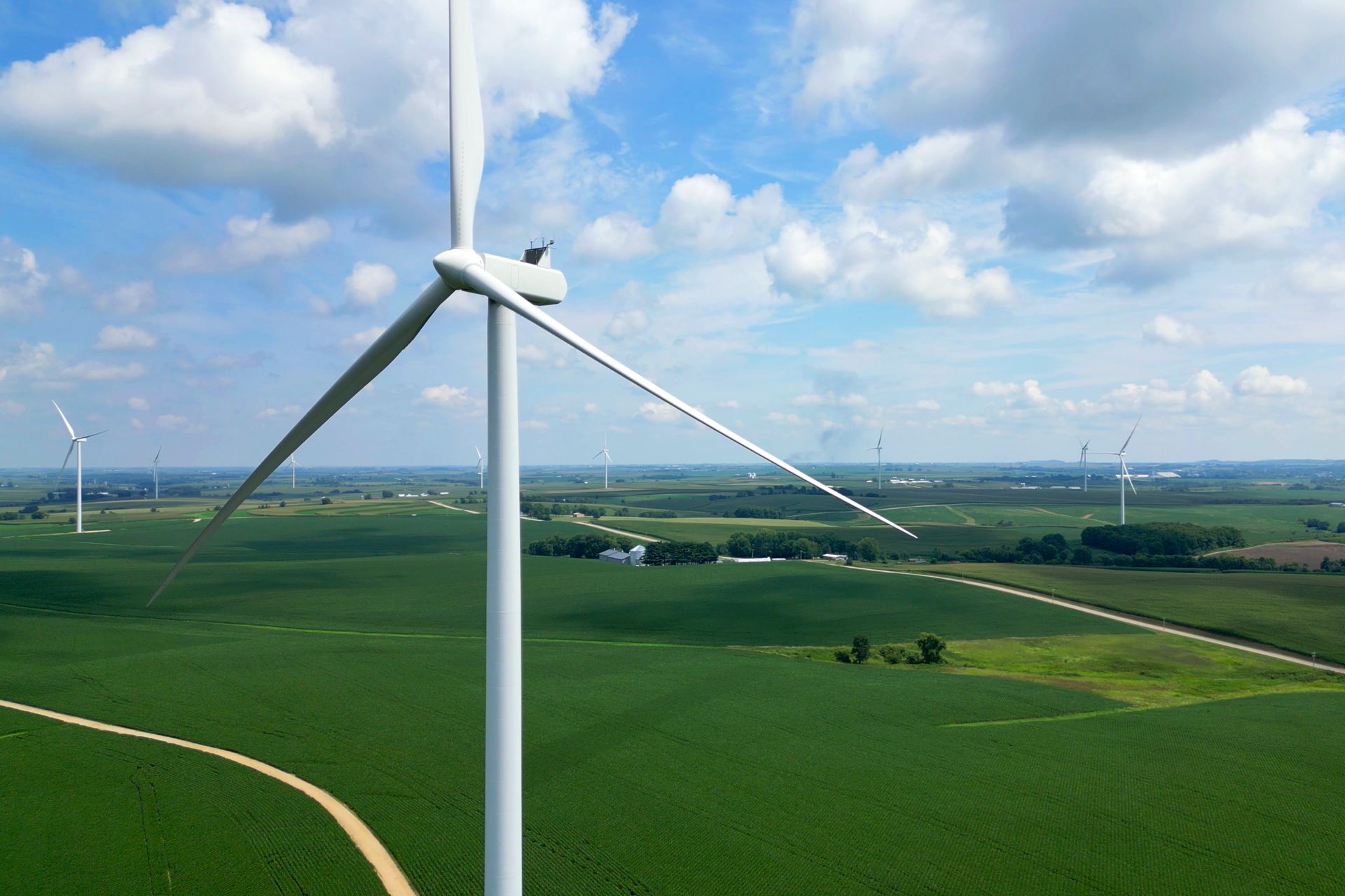 Wind turbines in a green field under a blue sky with fluffy clouds.
