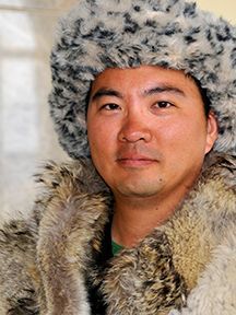 Man wearing a hat and light-colored shirt, looking directly at the camera with a slight smile.