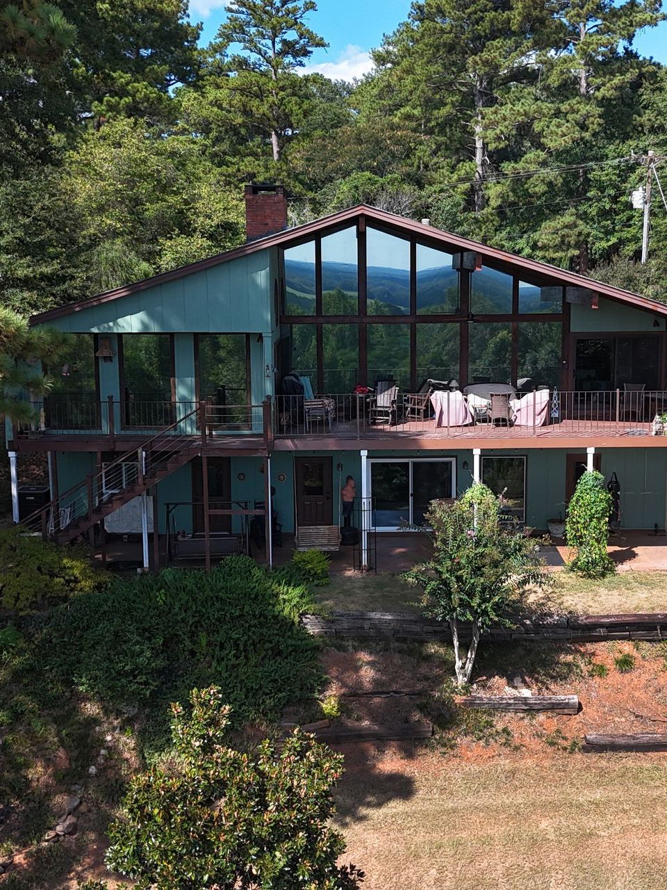Green house with large windows, deck, and a view of trees.