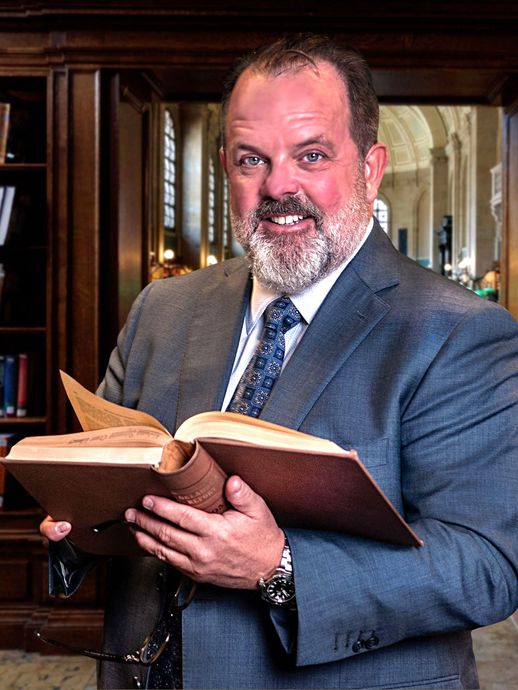 Man in suit holding open book, smiling in a library.