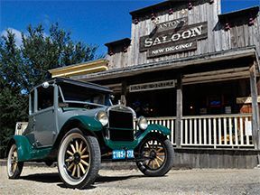 Vintage gray and green car parked outside Anton's Saloon, a wooden building with a porch.