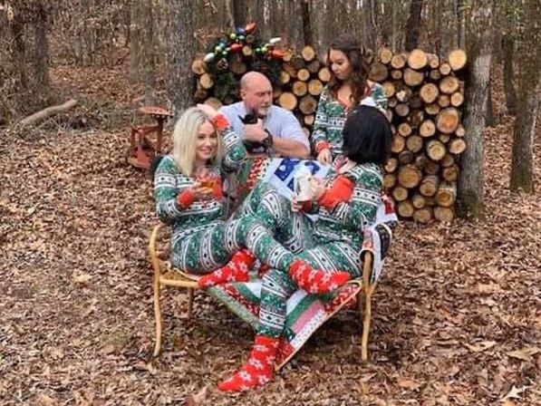 Family in matching pajamas sits outside in front of firewood.