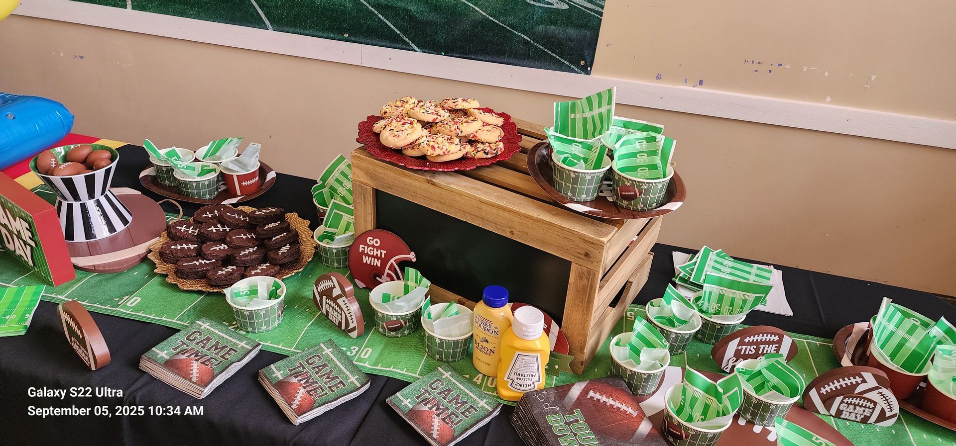 A table with football-themed treats, including cupcakes, cookies, and a cake.