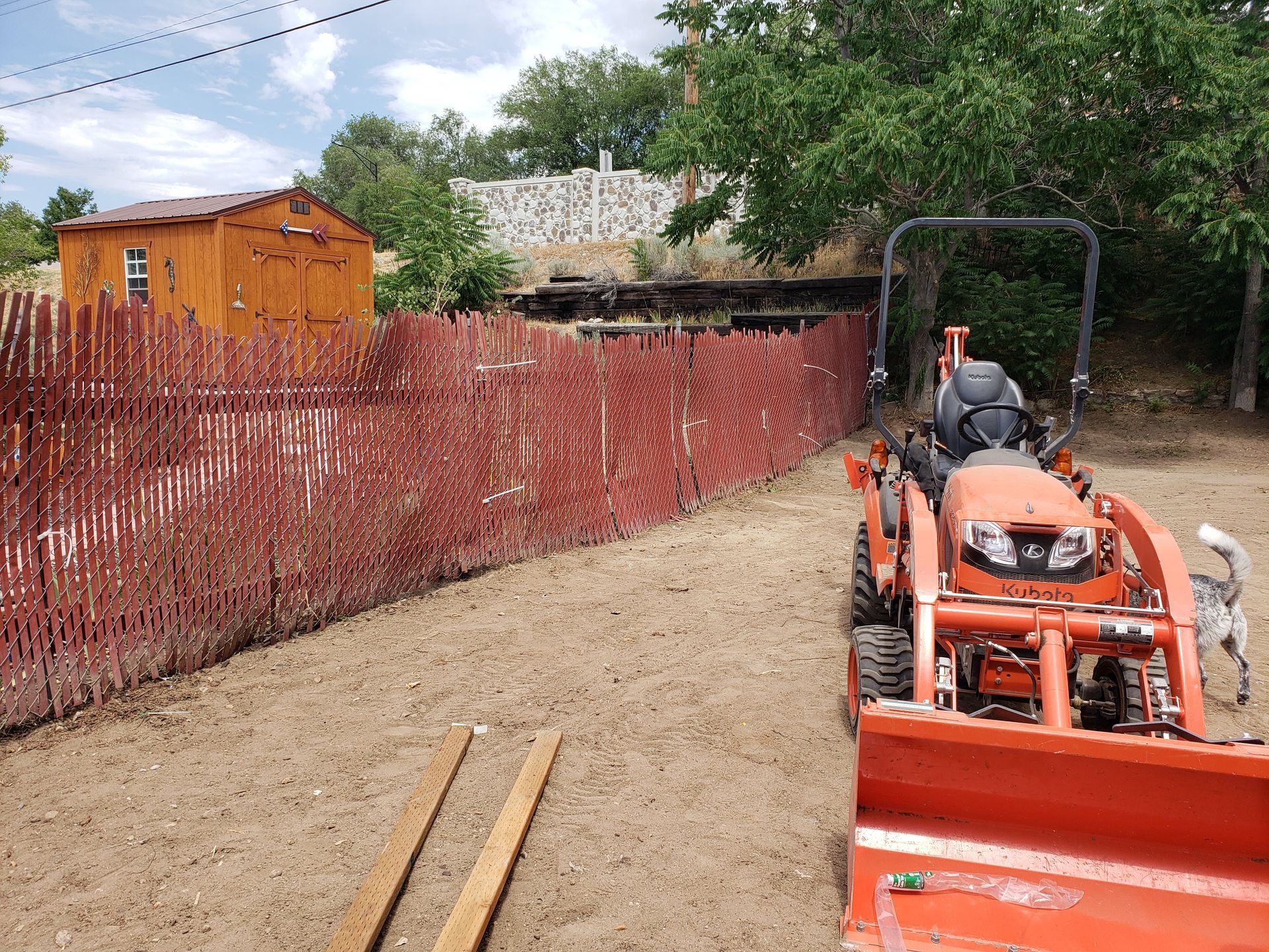 A small orange tractor is parked in front of a red fence.