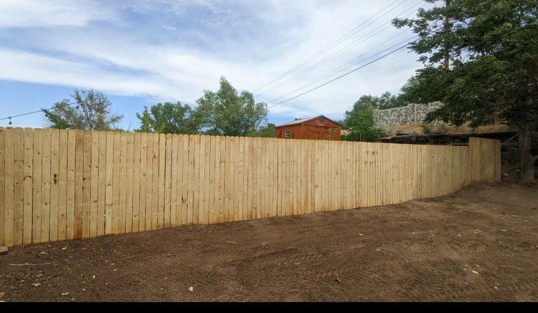 A wooden fence is in the middle of a dirt field.